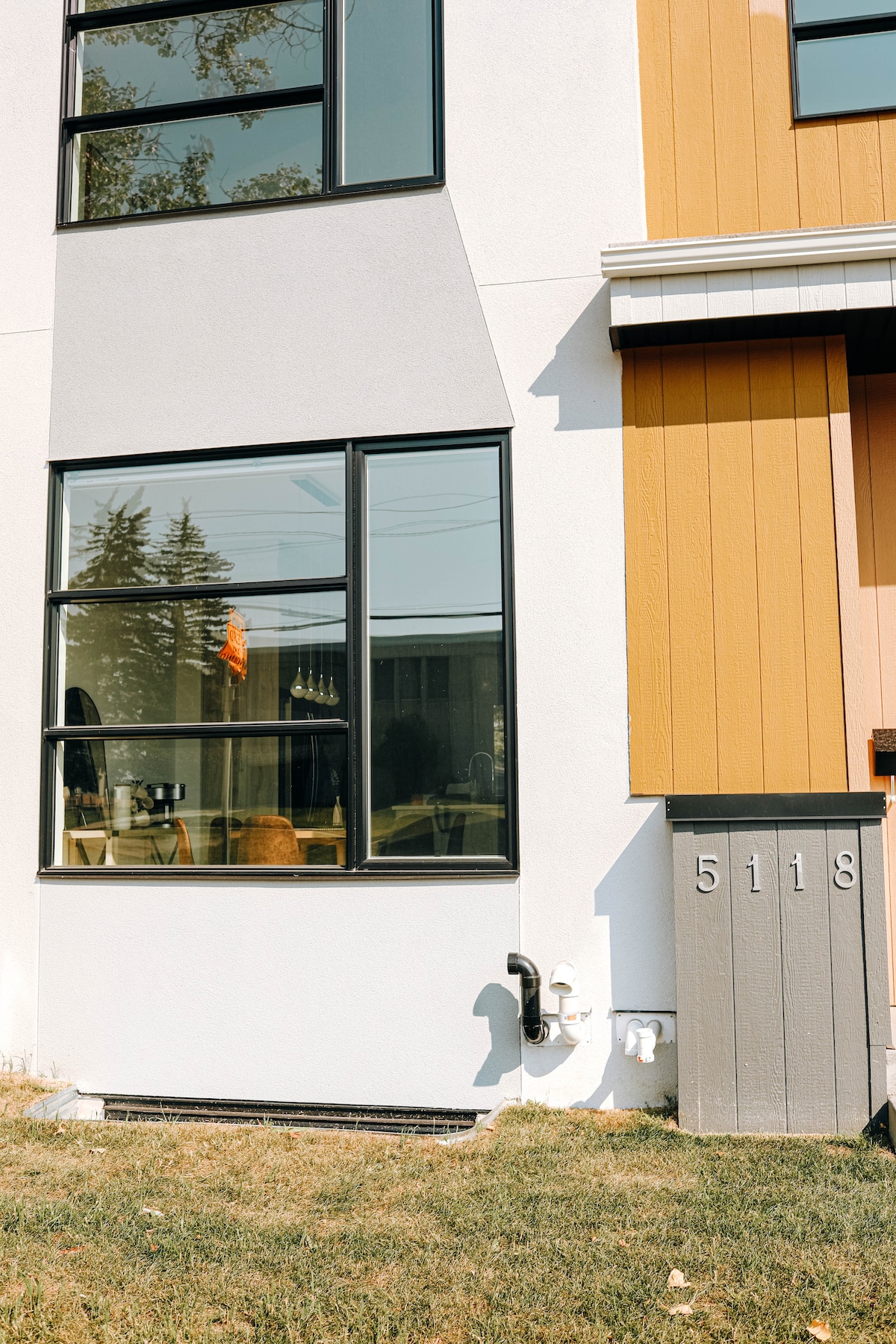 The exterior of the home features a mix of light and dark siding, showcasing large windows that provide ample natural light. A grey mailbox marked '5118' is situated by a patch of green grass, accentuating the modern architectural design.