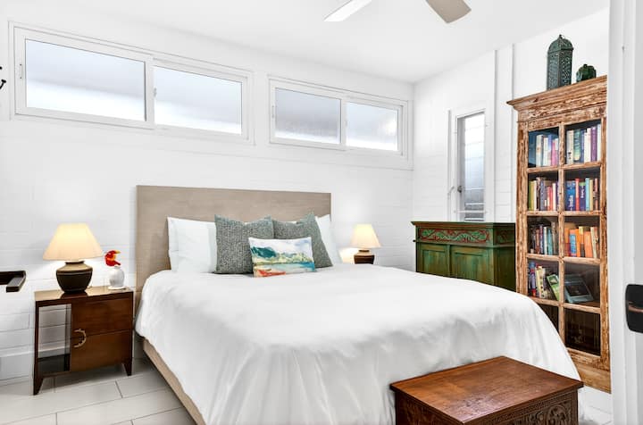 Sink into crisp white linens and let natural light brighten your mornings in this serene bedroom with curated books at your bedside.