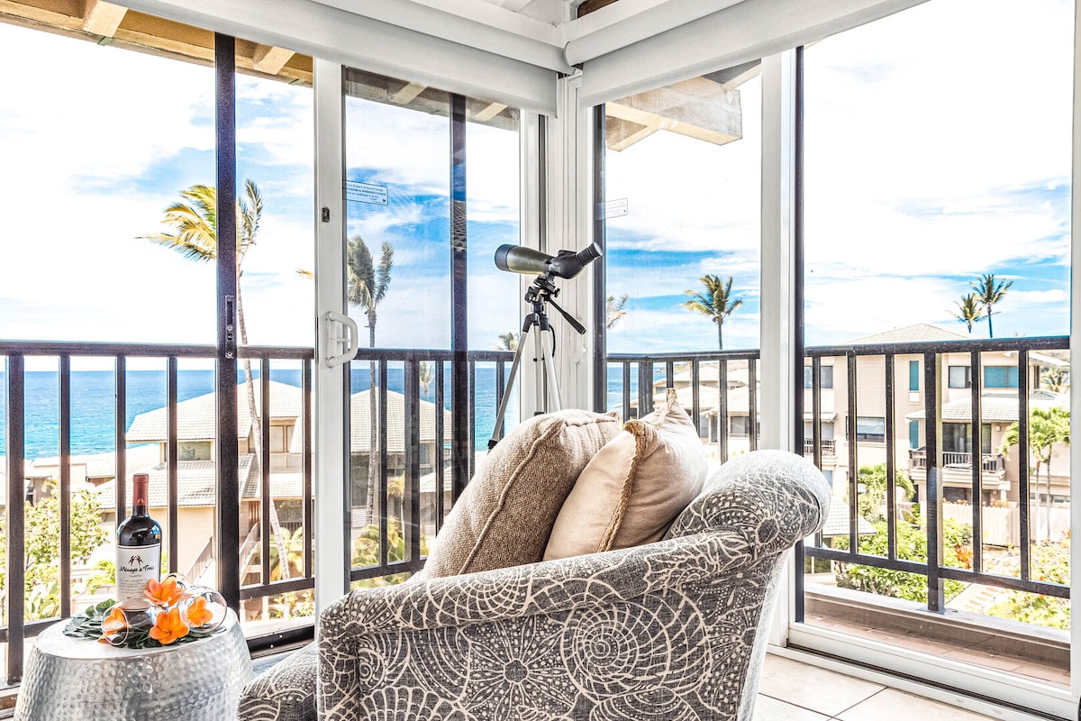 A comfortable armchair is positioned near large glass doors that offer panoramic ocean views. A small table holds a bottle of wine and a telescope, inviting relaxation and exploration. Palm trees sway gently outside, enhancing the serene coastal ambiance.