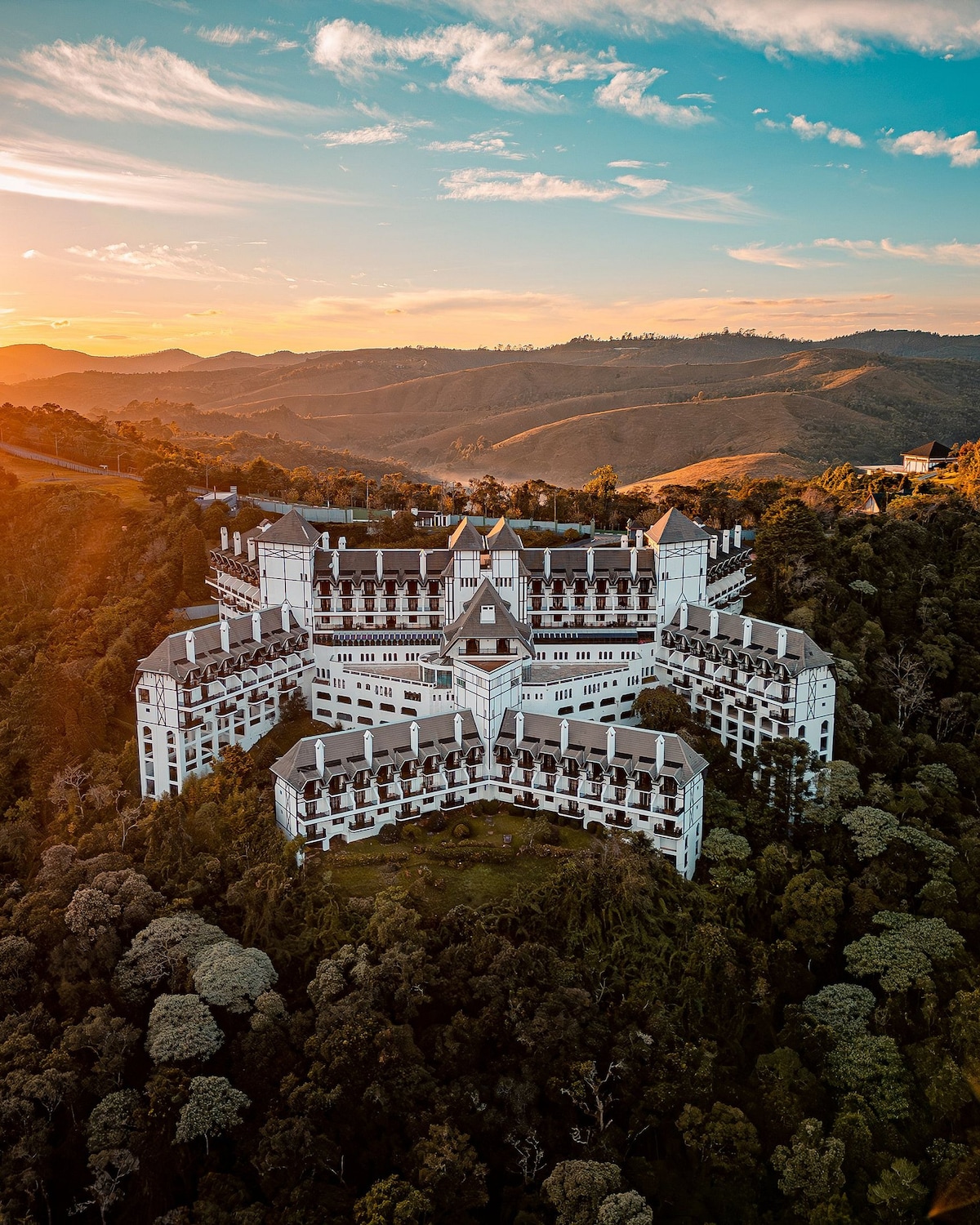 The exterior of Home Green Home castle is presented, showcasing a striking architecture with multiple angular wings. Surrounded by lush greenery, the structure is set against a backdrop of rolling hills under a colorful sunset sky.