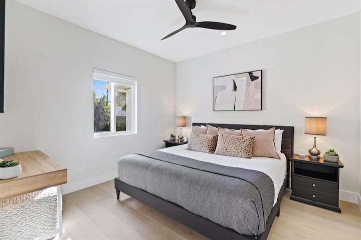 A calm bedroom with a king bed, desk, ceiling fan, and soft natural light gives guests a comfortable place to recharge.