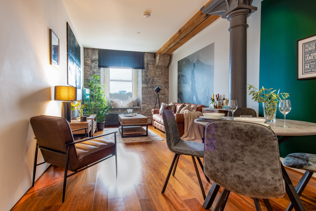 The living area features an inviting seating arrangement with a plush brown sofa and comfortable chairs, complemented by a stylish dining table. Large windows allow natural light to illuminate the space, highlighting a mix of contemporary and rustic elements, including warm wooden flooring.