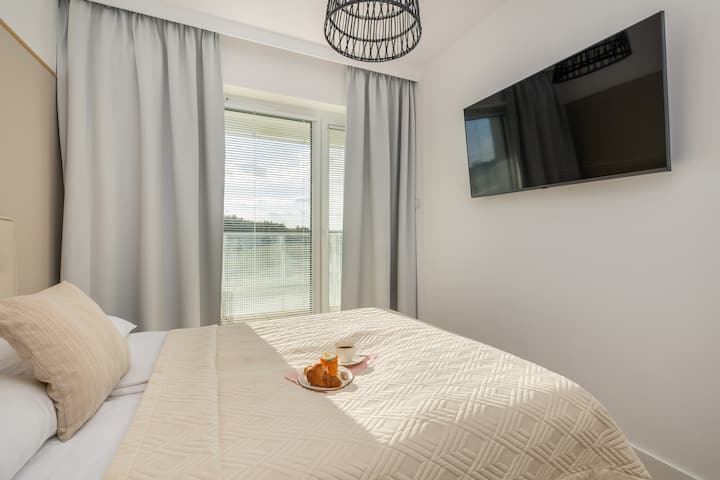 Un dormitorio luminoso y acogedor con cortinas transparentes, una cama cómoda y una decoración sencilla y moderna.