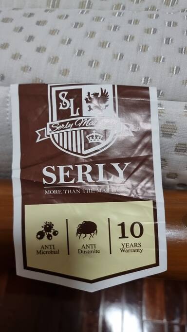 A close-up view of a mattress label, displaying features such as 'Anti Microbial' and 'Anti Dustmite,' which ensures comfort and hygiene. The label also indicates a 10-year warranty, emphasizing the quality of the mattress. The background shows a patterned fabric.