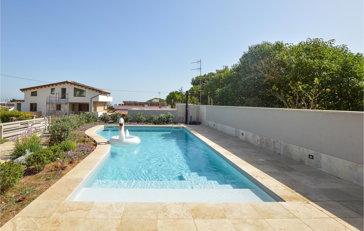 A serene outdoor space features a private pool with clear water, surrounded by a spacious stone deck. Lush greenery lines the perimeter, enhancing the tranquil atmosphere. An inflatable swan adds a touch of whimsy to the pool, inviting relaxation and enjoyment.