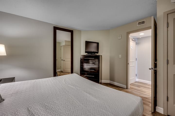  një dhomë gjumi me një krevat, një televizor me ekran të sheshtë, një pasqyrë dhe një dollap. Dhoma ka tone neutrale, me dysheme të lehta prej druri dhe një derë që të çon jashtë.