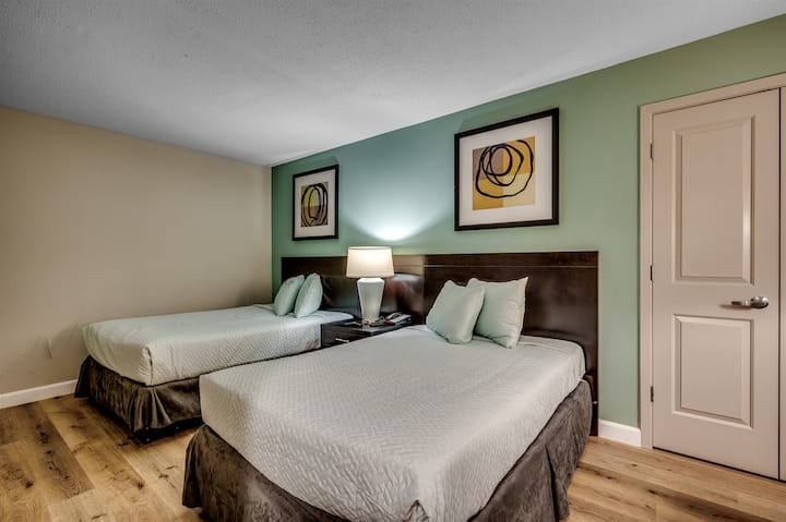 Një dhomë gjumi e rehatshme me dy krevate, ndriçim të butë dhe vepra arti moderne, duke krijuar një atmosferë të ngrohtë dhe ftuese.