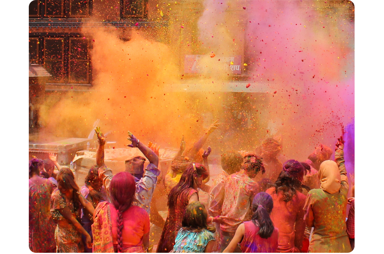 Festival Holi di India. Sekelompok besar orang, di tengah perayaan, terlihat dari belakang di tengah kabut warna-warni merah muda, oranye, dan ungu.