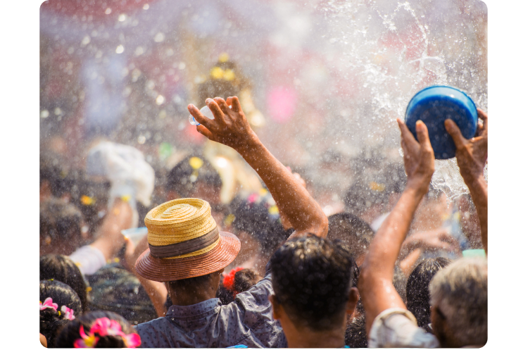 Festival Songkran di Thailand. Sekelompok besar orang yang membelakangi kita, mengangkat lengan mereka sambil memegang ember dan botol lalu menyiramkan air ke segala arah, membasahi semua orang.