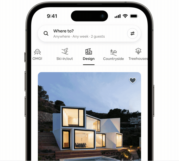 An animated gif of a phone opens to the categories section of the Airbnb app. It cycles between categories, showing different homes. We start on the Design Category with a home that looks as if it has been built with white blocks. Large open windows show light coming from inside. It slides to the left and we’re on the Treehouse Category. A small black house with a slanted roof is held up between trees, accessible via wood stairs and a deck. It swipes to the left and shows the Countryside Category, with a small log cabin in a flowery field and snowy mountains in the background.